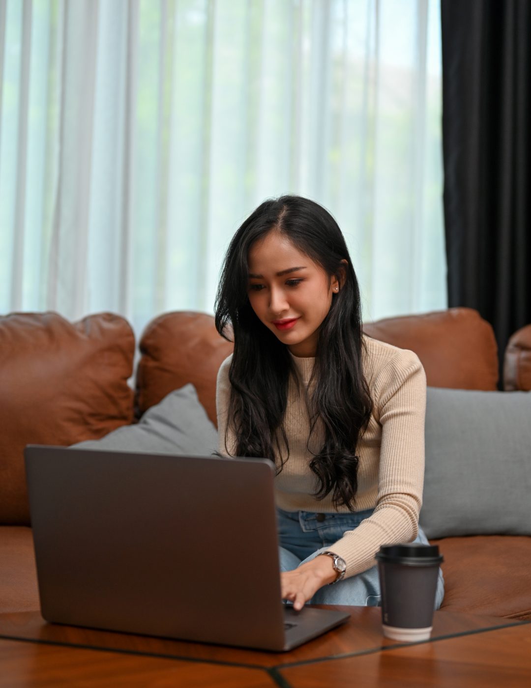 Portrait, Attractive young Asian female concentrating working on her project on laptop computer while sitting in her modern vintage living room.