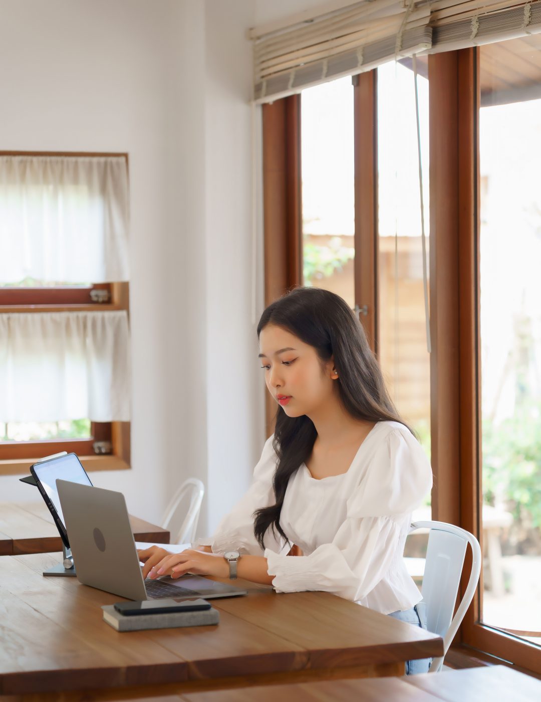 Young asian businesswoman reading marketing data of business on tablet and typing information on laptop while analysis strategy about investment and planning of new startup project to working in cafe.